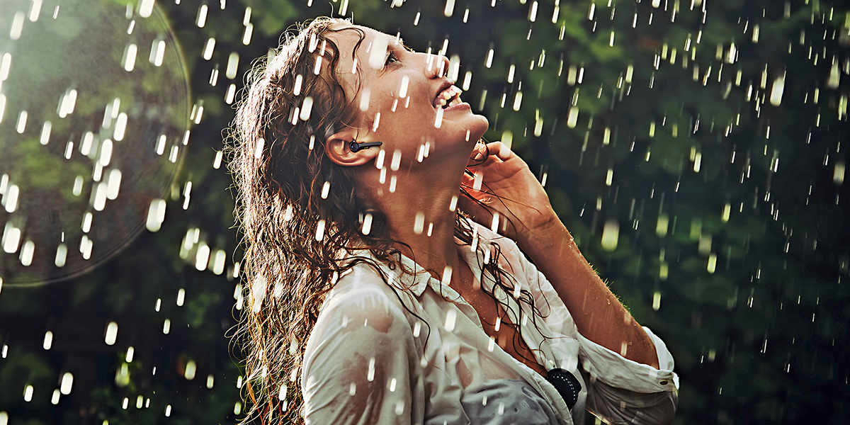 A woman caught in the rain with no umbrella is talking on a headset protected by a GORE® Acoustic Vent.