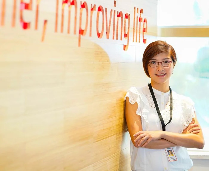 An Associate standing in front of a wall that says Together, improving life.