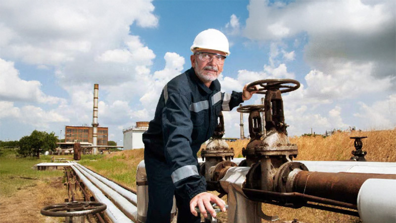 Worker fixing a long pipe on a field while wearing PPE.