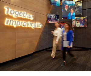 Two Associates walking next to a wall with "Together, improving life" on it.